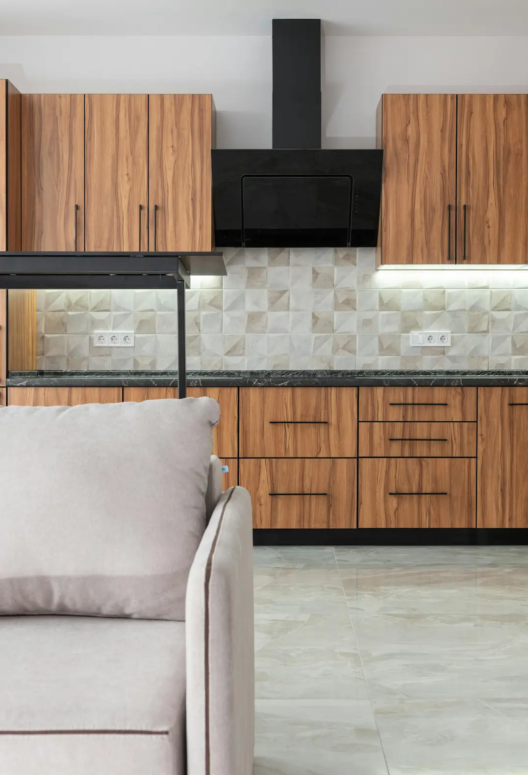 Stylish contemporary kitchen with wooden cabinets and a comfortable sofa, offering elegance and functionality.